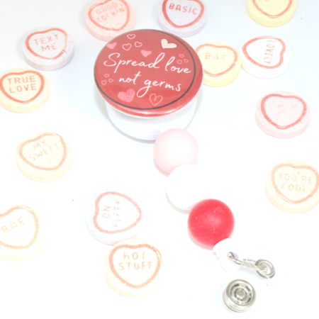 Nurse badge reel has a red circle top that says Spread love not germs. Bottom has 3 beads, pink, white and red. Surrounded by candy hearts.