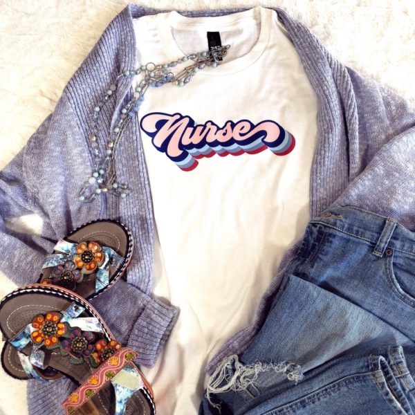 Blue cardiagan sweater with white tshirt that says nurse in retro font with long blue necklace, jeans and sandals