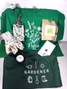 Garden Nurse Goddess subscription box, floral nurse tee, gardener apron, birth flower necklace, gardening gloves, basil in a bag, hummingbird seeds, garden badge reel